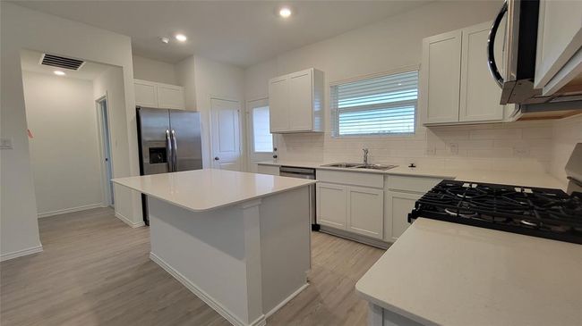 Kitchen featuring a kitchen island, decorative backsplash, light wood-style floors, light countertops, and stainless steel refrigerator with ice dispenser | Image 4