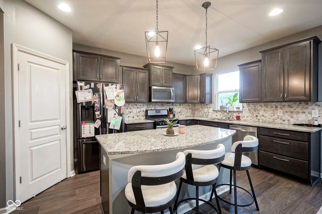 kitchen with appliances with stainless steel finishes, dark brown cabinetry, a kitchen island, decorative backsplash, and light stone countertops | Image 15