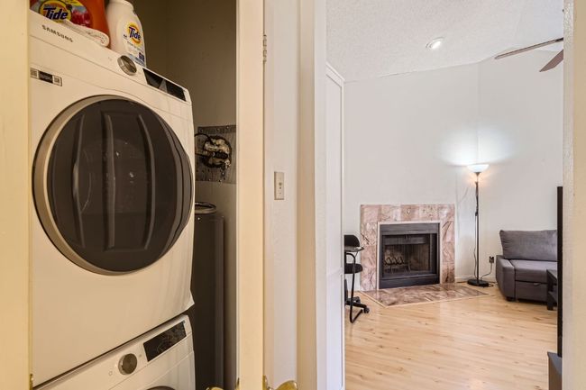 Washroom featuring light wood finished floors, a fireplace, stacked washer and clothes dryer, laundry area, and a ceiling fan | Image 22