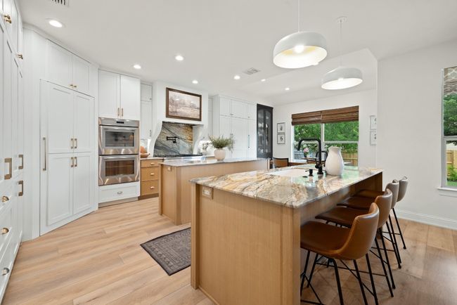 Kitchen with a kitchen island with sink, a sink, light wood finished floors, and double oven | Image 16