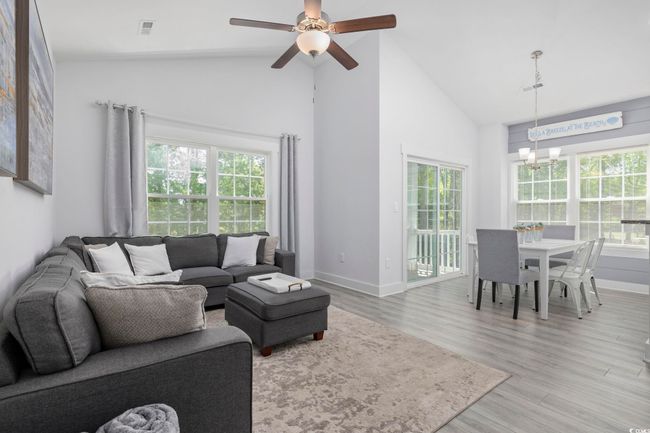 Living area with a healthy amount of sunlight, light wood finished floors, visible vents, and ceiling fan with notable chandelier | Image 8