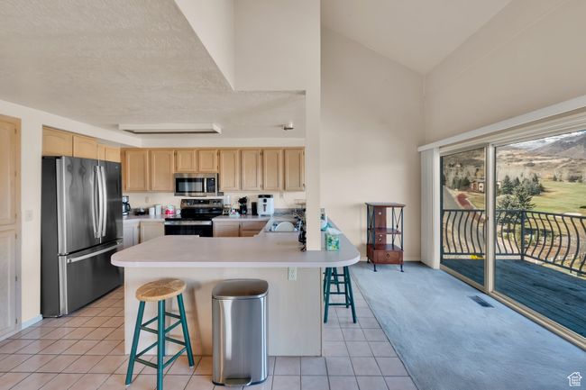 Kitchen with light countertops, a sink, a breakfast bar, light brown cabinetry, and stainless steel appliances | Image 9
