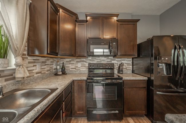 kitchen featuring black appliances, a sink, wood finished floors, decorative backsplash, and light countertops | Image 20