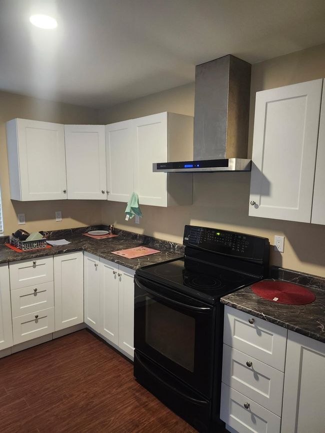 Kitchen with black / electric stove, wall chimney exhaust hood, and white cabinets | Image 7