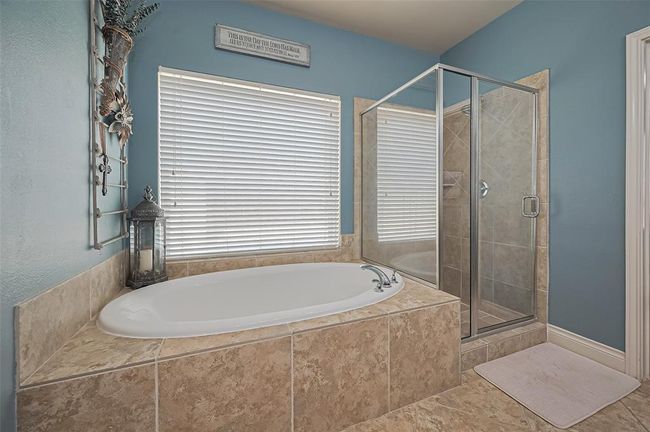 Opposite the vanity, the soaking tub is perfectly positioned under a generous window, accompanied by a walk-in shower featuring a calming neutral tile surround. | Image 25