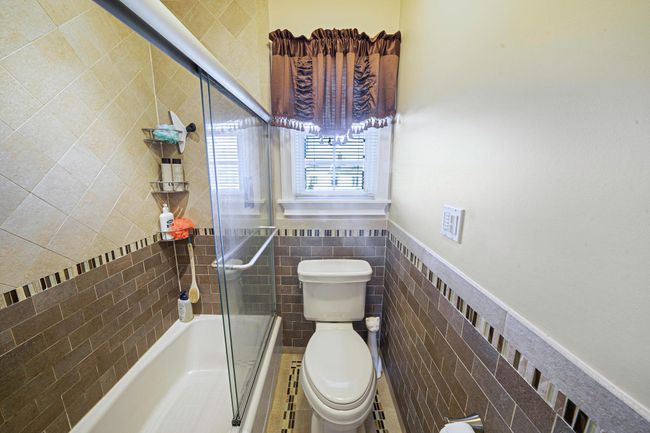 Bathroom with tile walls, combined bath / shower with glass door, toilet, and wainscoting | Image 24
