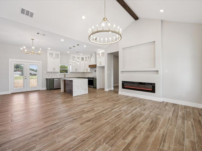 Unfurnished living room featuring a chandelier, beam ceiling, light wood-style floors, a glass covered fireplace, and high vaulted ceiling | Image 6