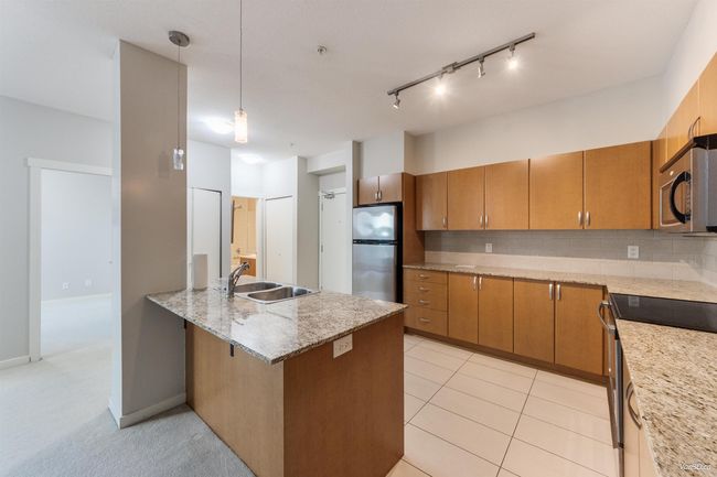 Kitchen featuring appliances with stainless steel finishes, hanging light fixtures, light stone countertops, decorative backsplash, and a kitchen bar | Image 6