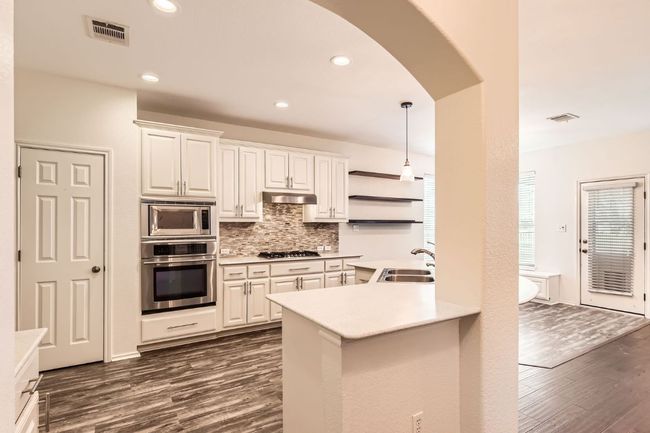 Kitchen featuring stainless steel appliances, dark wood-type flooring, arched walkways, backsplash, and light countertops | Image 14