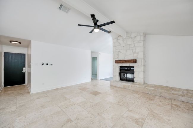 Unfurnished living room with lofted ceiling with beams, visible vents, tile patterned floors, a ceiling fan, and a stone fireplace | Image 8