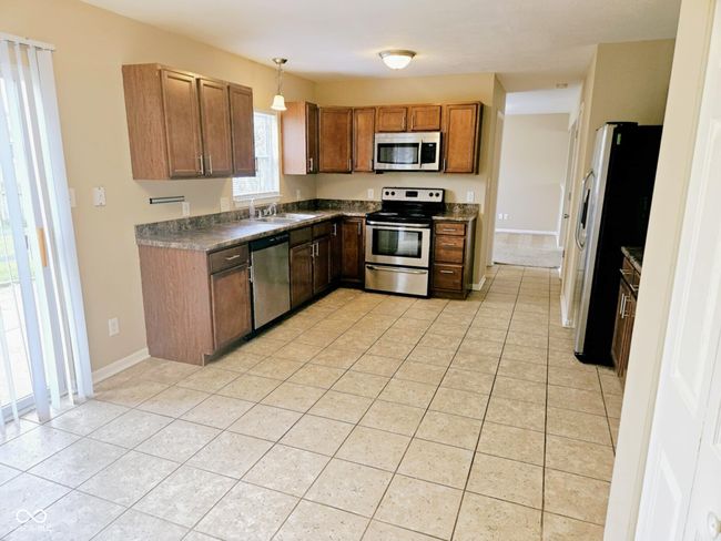 kitchen featuring brown cabinets, a sink, light tile patterned floors, dark countertops, and appliances with stainless steel finishes | Image 18