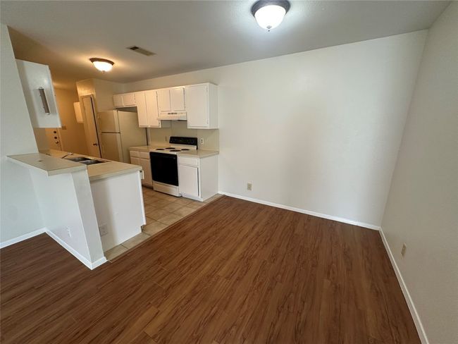 Kitchen with white appliances, under cabinet range hood, wood finished floors, light countertops, and a peninsula | Image 6