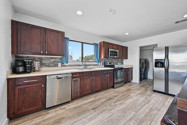 Kitchen with stainless steel appliances, washing machine and dryer, a sink, light wood-style flooring, and light countertops | Image 15