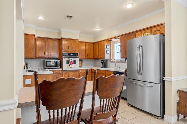 Kitchen featuring appliances with stainless steel finishes, brown cabinetry, ornamental molding, light countertops, and light tile patterned floors | Image 9