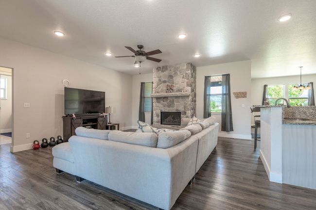Living area featuring a stone fireplace, a ceiling fan, dark wood finished floors, recessed lighting, and a textured ceiling | Image 7