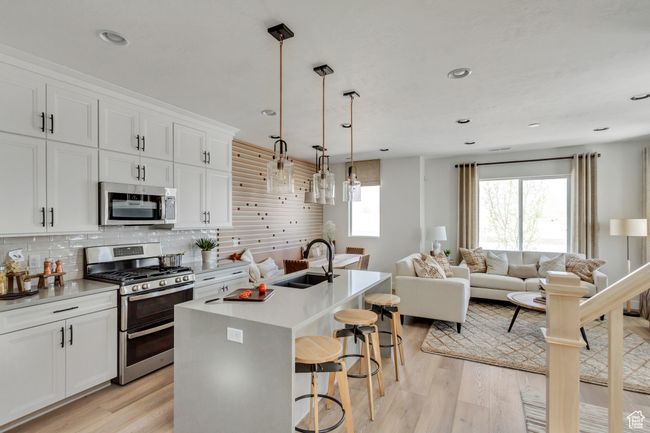 Kitchen featuring stainless steel appliances, light wood-style flooring, a breakfast bar area, open floor plan, and decorative backsplash | Image 38