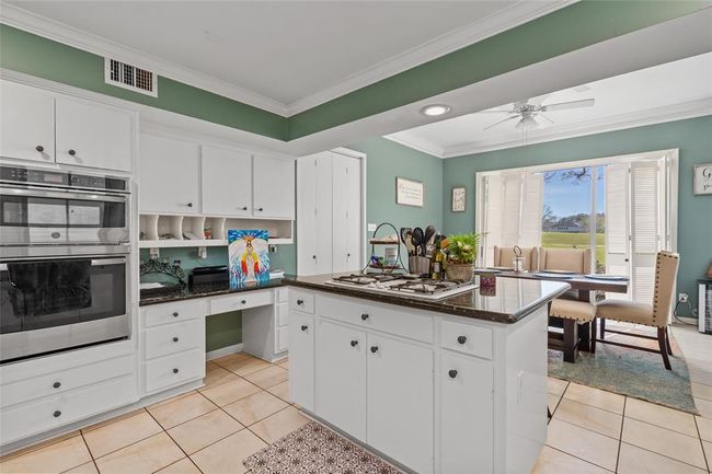 This inviting kitchen features ample cabinetry, a built-in oven, and a spacious island with a gas cooktop. The convenient built-in desk area offers additional storage and workspace. Large windows in the adjacent dining area provide stunning views, filling the space with natural light. | Image 19