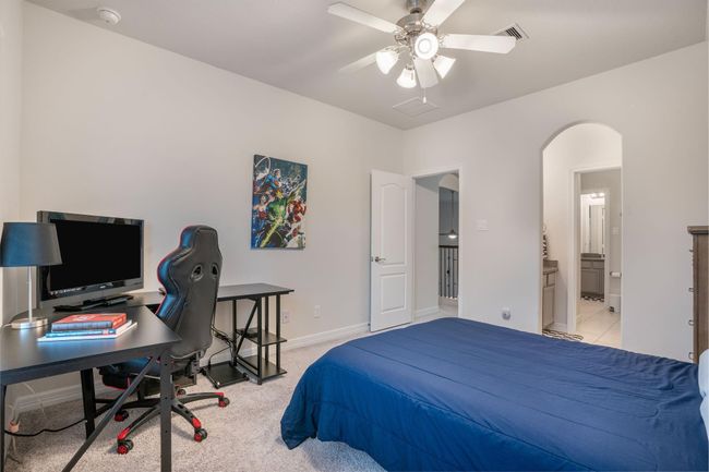 A cozy bedroom with carpeted flooring, a ceiling fan and an adjoining en-suite bathroom visible through an arched doorway, providing convenience. | Image 34