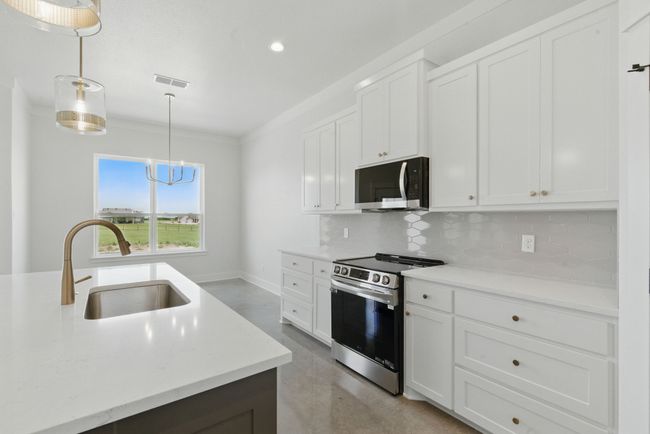 Kitchen with stainless steel appliances, a sink, finished concrete floors, decorative backsplash, and white cabinetry | Image 8