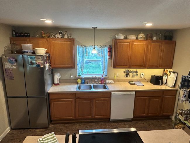 Kitchen with freestanding refrigerator, white dishwasher, light countertops, pendant lighting, and brown cabinetry | Image 17