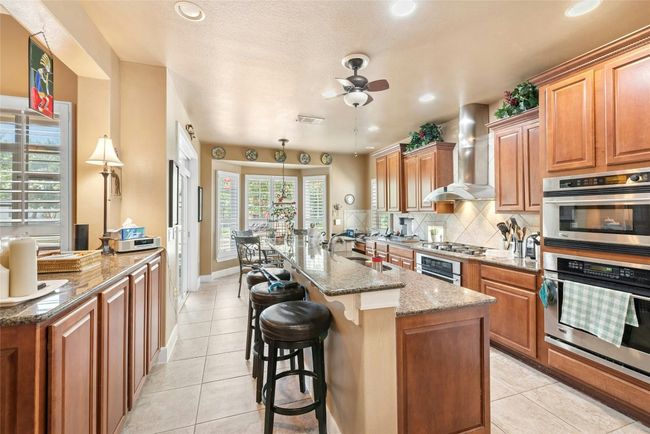 Kitchen featuring wall chimney range hood, stainless steel appliances, ceiling fan, stone countertops, and decorative backsplash | Image 6