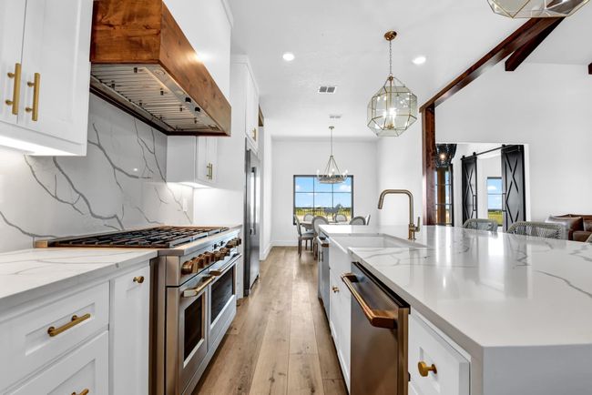 Kitchen with backsplash, a chandelier, high quality appliances, exhaust hood, and white cabinetry | Image 8