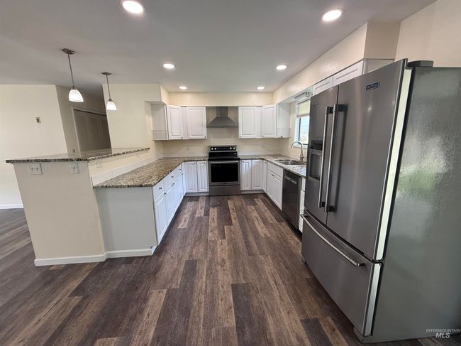 Kitchen featuring stainless steel appliances, wall chimney exhaust hood, a peninsula, dark wood-style flooring, and stone counters | Image 16
