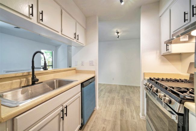 Kitchen featuring dishwashing machine, stainless steel gas range oven, under cabinet range hood, light wood-style flooring, and white cabinetry | Image 11