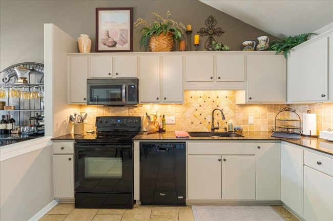 Kitchen with tasteful backsplash, vaulted ceiling, white cabinets, black appliances, and a sink | Image 11