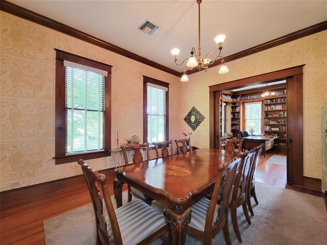 Elegant formal dining room with rich wood trim, an antique chandelier, and hardwood floors—ideal for entertaining. | Image 9