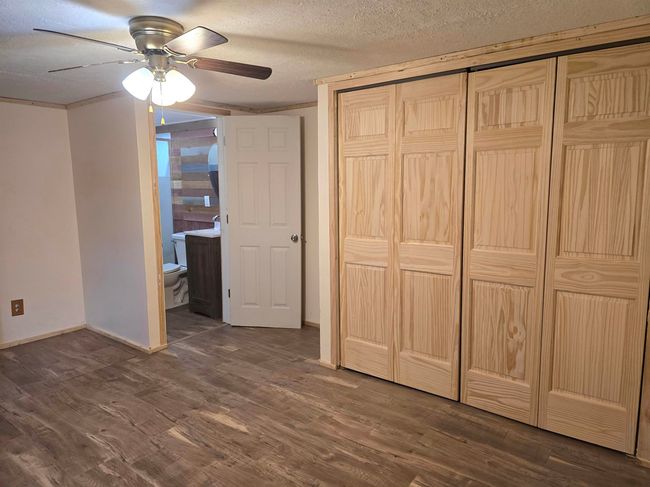 Unfurnished bedroom with a closet, a textured ceiling, dark wood-type flooring, ensuite bathroom, and ceiling fan | Image 11