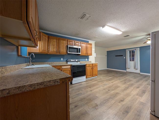 Kitchen with a sink, black range with electric stovetop, stainless steel microwave, visible vents, and freestanding refrigerator | Image 7