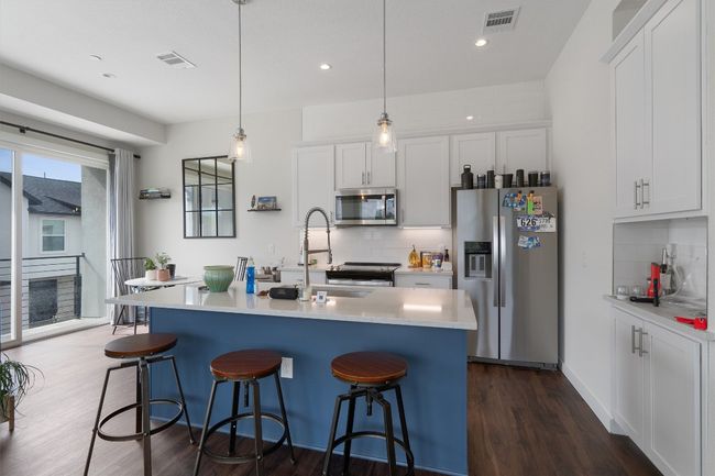 Kitchen featuring appliances with stainless steel finishes, backsplash, a breakfast bar, dark wood-type flooring, and light countertops | Image 21