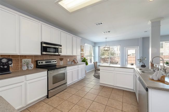 Kitchen with light tile patterned floors, appliances with stainless steel finishes, backsplash, hanging light fixtures, and a sink | Image 5