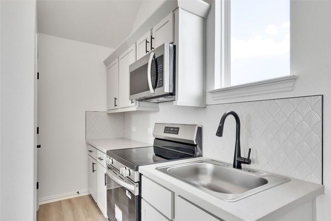 Kitchen with stainless steel appliances, backsplash, light countertops, light wood-style floors, and white cabinetry | Image 16