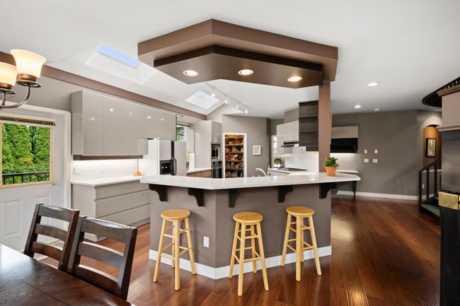 Kitchen with dark wood finished floors, a breakfast bar area, a peninsula, a skylight, and white fridge with ice dispenser | Image 12