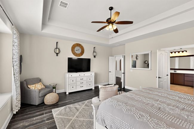 Bedroom featuring baseboards, a tray ceiling, wood finished floors, and connected bathroom | Image 14