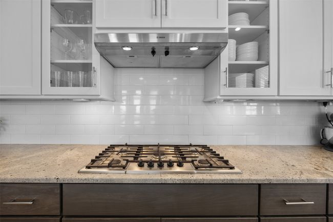 Kitchen with extractor fan, stainless steel gas cooktop, glass insert cabinets, tasteful backsplash, and white cabinets | Image 8