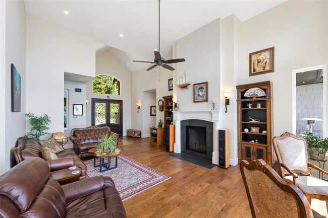Living area with high vaulted ceiling, wood finished floors, a tile fireplace, ceiling fan, and recessed lighting | Image 37