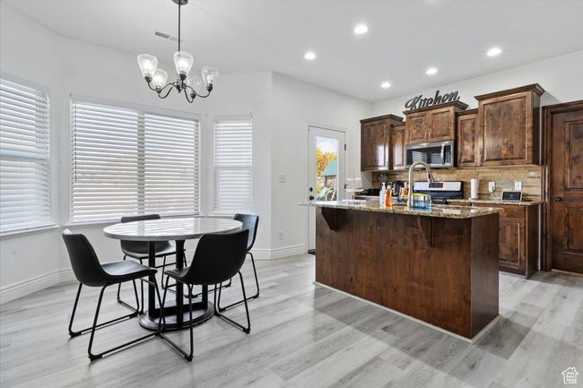 Kitchen featuring a center island with sink, light stone counters, decorative backsplash, a chandelier, and light hardwood / wood-style flooring | Image 7