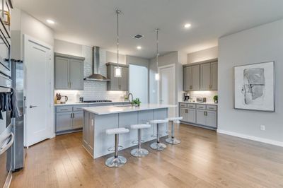 Kitchen with light hardwood / wood-style floors, a kitchen breakfast bar, an island with sink, wall chimney range hood, and pendant lighting | Image 3