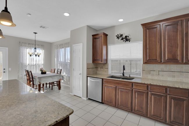 Kitchen featuring light tile patterned floors, visible vents, dishwasher, decorative light fixtures, and a sink | Image 15