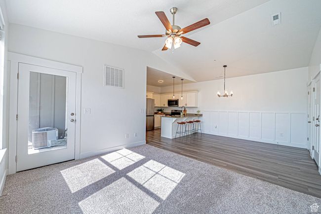 Unfurnished living room featuring visible vents, dark colored carpet, vaulted ceiling, and ceiling fan with notable chandelier | Image 6