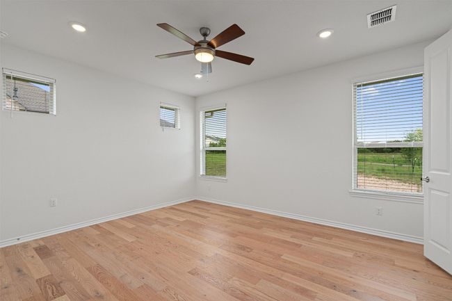 Primary bedroom features windows with a view of the reserve & walking trail in the distance. Wood floors, recessed lighting and a ceiling fan. | Image 11