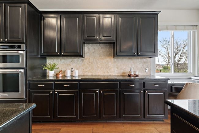 Kitchen featuring stainless steel double oven, decorative backsplash, light wood finished floors, and dark stone counters | Image 19
