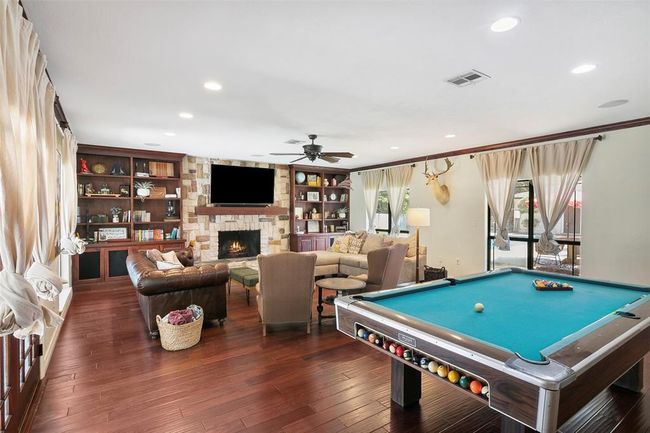 Spacious living room with hardwood floors, featuring a cozy fireplace, built-in bookshelves, and a pool table. Large windows provide natural light, and the room is stylishly furnished for relaxation and entertainment. | Image 10