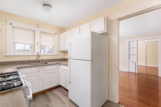 Kitchen featuring white cabinets, light wood finished floors, a sink, and white appliances | Image 6