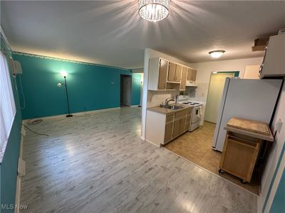 Dining room & kitchen featuring white appliances, sink, light LVT flooring, backsplash, and beautiful light fixture. | Image 3