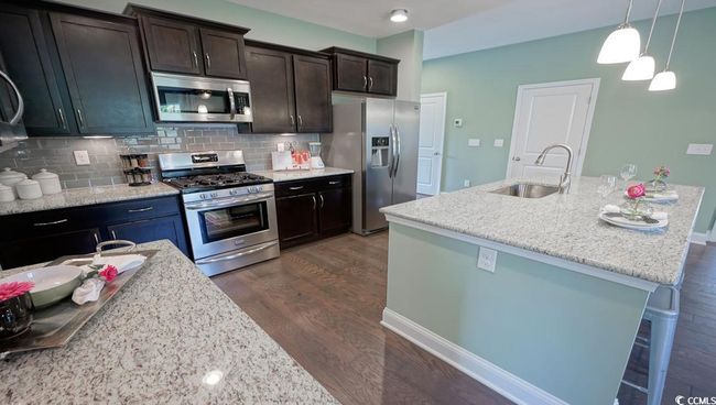 Kitchen featuring stainless steel appliances, a sink, dark wood-type flooring, decorative backsplash, and pendant lighting | Image 7