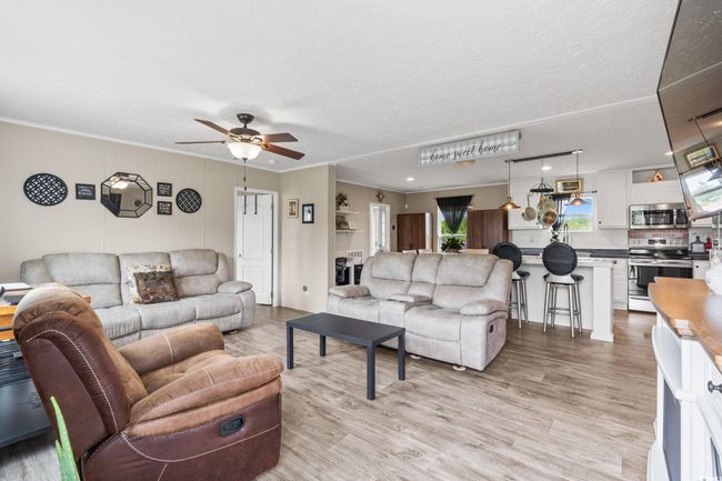 Living room with ceiling fan, light wood finished floors, crown molding, and a textured ceiling | Image 8
